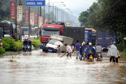 5月18日，國道324線廣西興業(yè)縣石南鎮(zhèn)黑石嶺路段被洪水淹沒，一名群眾手持木棍為摩托車探路。