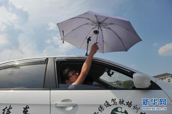 7月20日，在浙江省臨安市一家駕校內(nèi)，一名學(xué)員在車(chē)頂架著遮陽(yáng)傘的教練車(chē)內(nèi)練習(xí)。